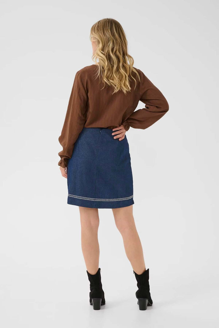 Femme portant la Jupe Gro en denim avec broderies florales, coupe droite au-dessus du genou, look bohème chic.