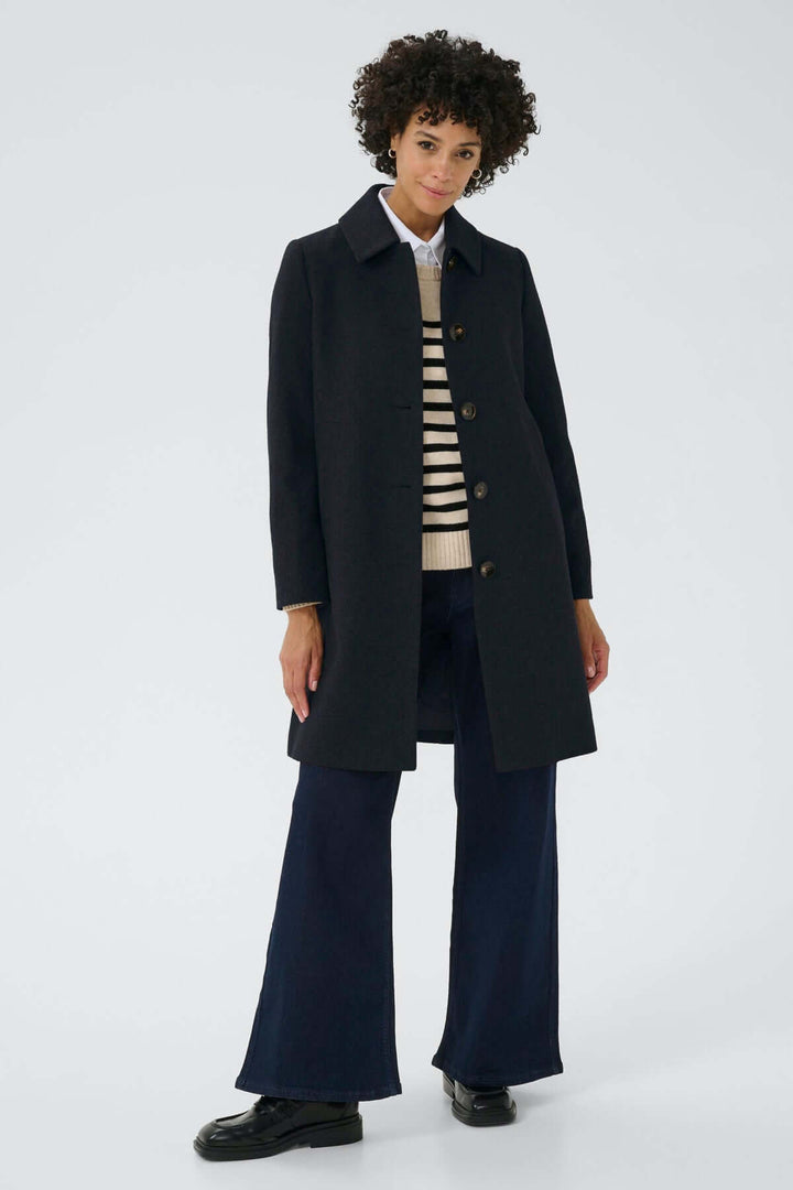 Femme portant le Manteau en laine Kamillas noir avec col chemise, coupe droite, et pantalon habillé, style chic et sophistiqué.