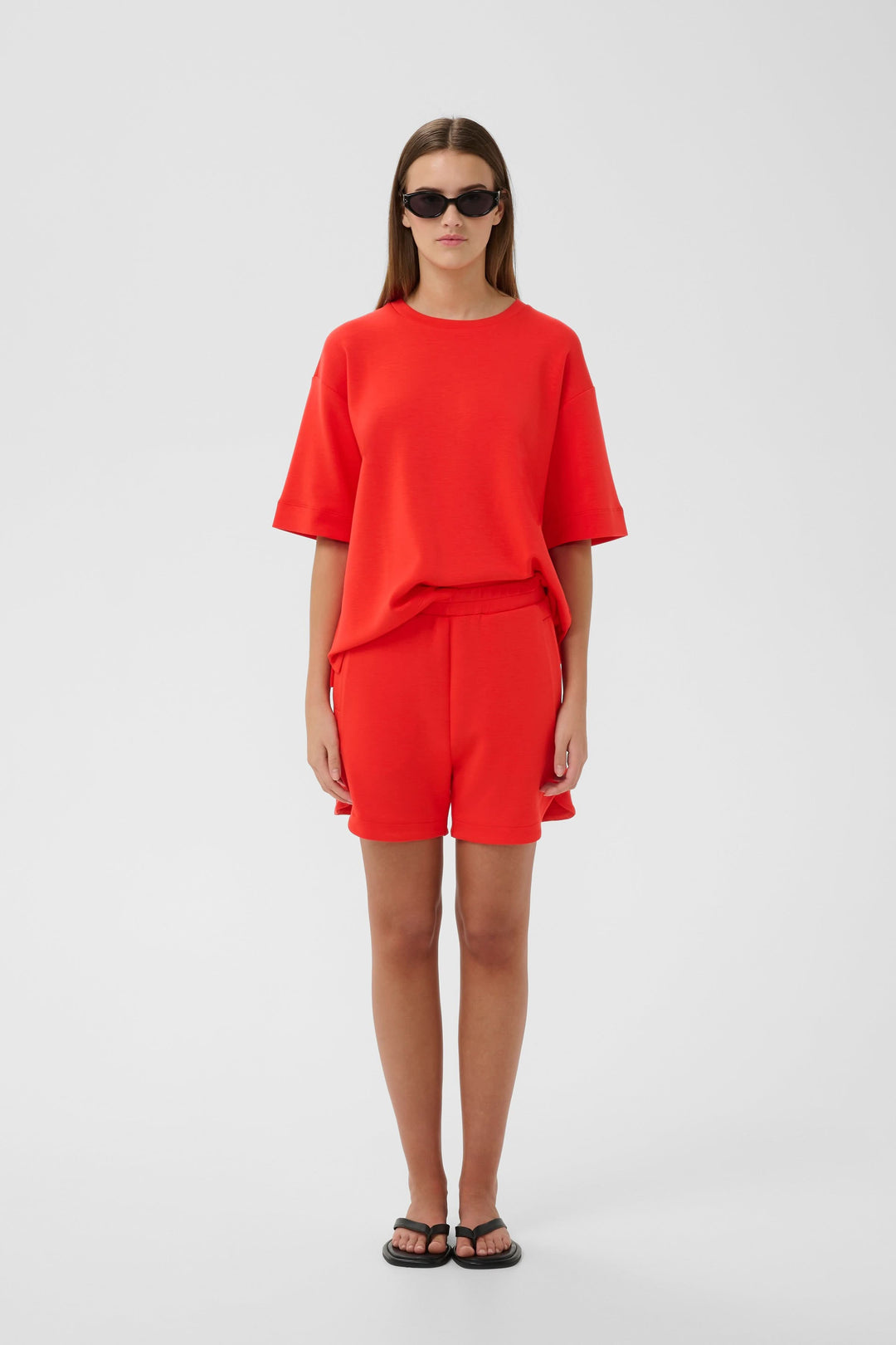 Femme portant Bermuda Hennieh en molleton rouge avec t-shirt assorti, coupe droite au-dessus du genou, style minimaliste.
