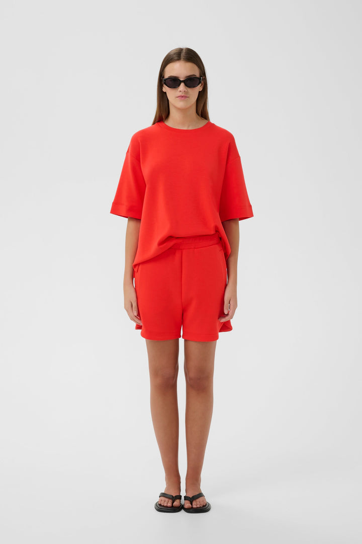Femme portant Bermuda Hennieh en molleton rouge avec t-shirt assorti, coupe droite au-dessus du genou, style minimaliste.
