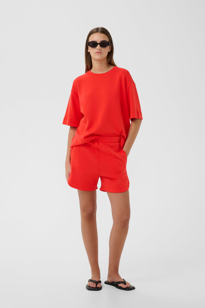 Femme portant le Bermuda Hennieh en molleton rouge, style décontracté avec taille élastique et poches latérales, pour confort optimal.