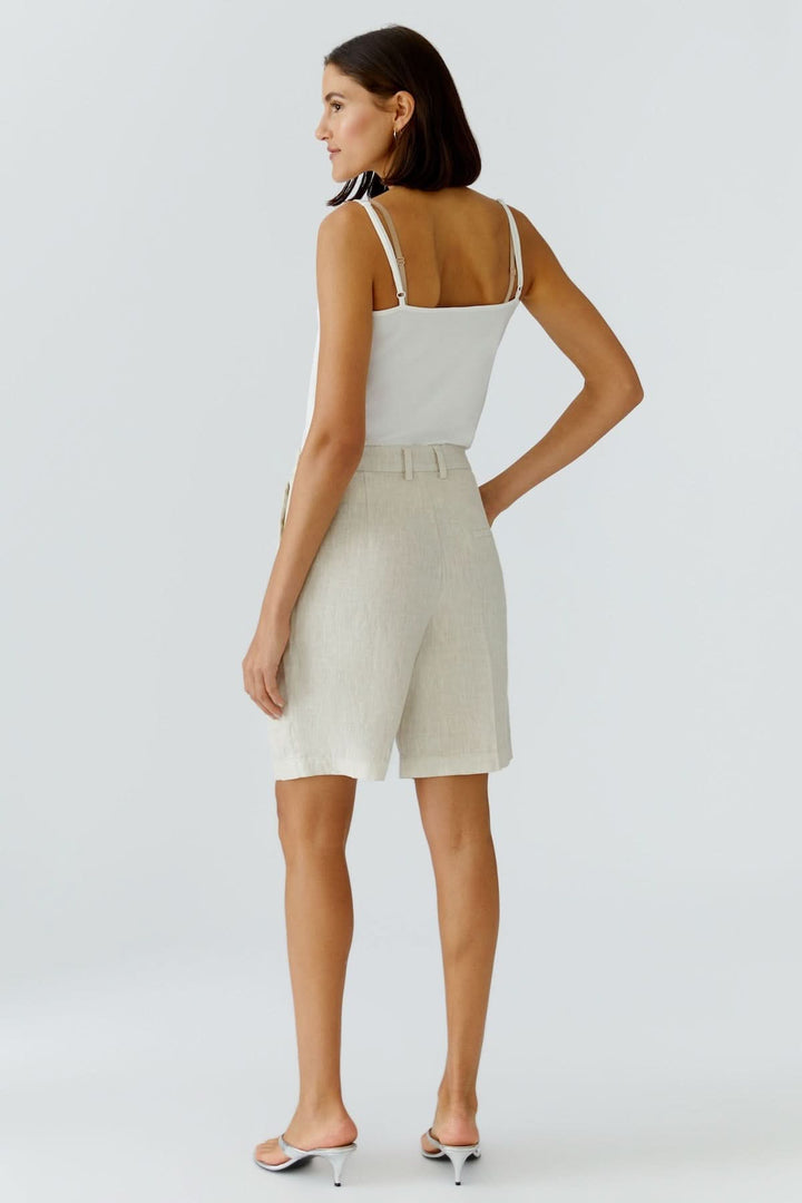 Femme portant un Bermuda en lin beige, coupe droite élégante, associée à un haut blanc pour une tenue estivale chic et confortable.