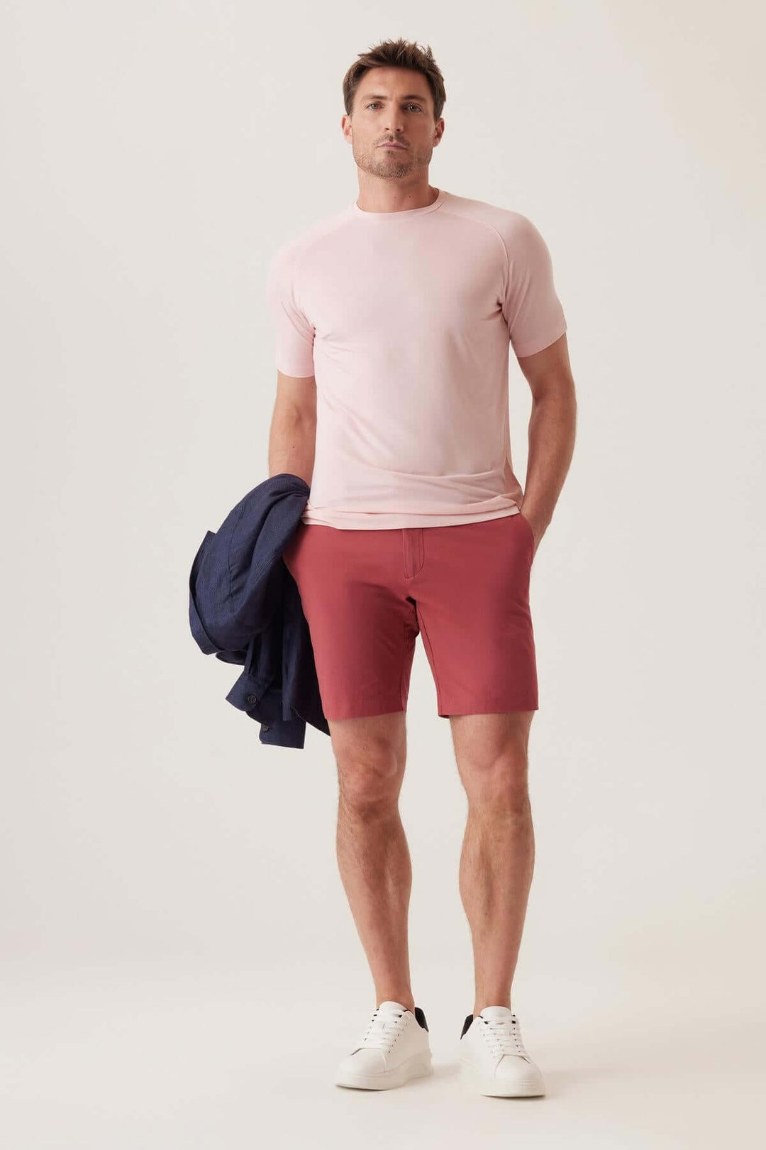 Homme portant un t-shirt rose et un short rouge, avec une veste bleue, style décontracté et moderne.