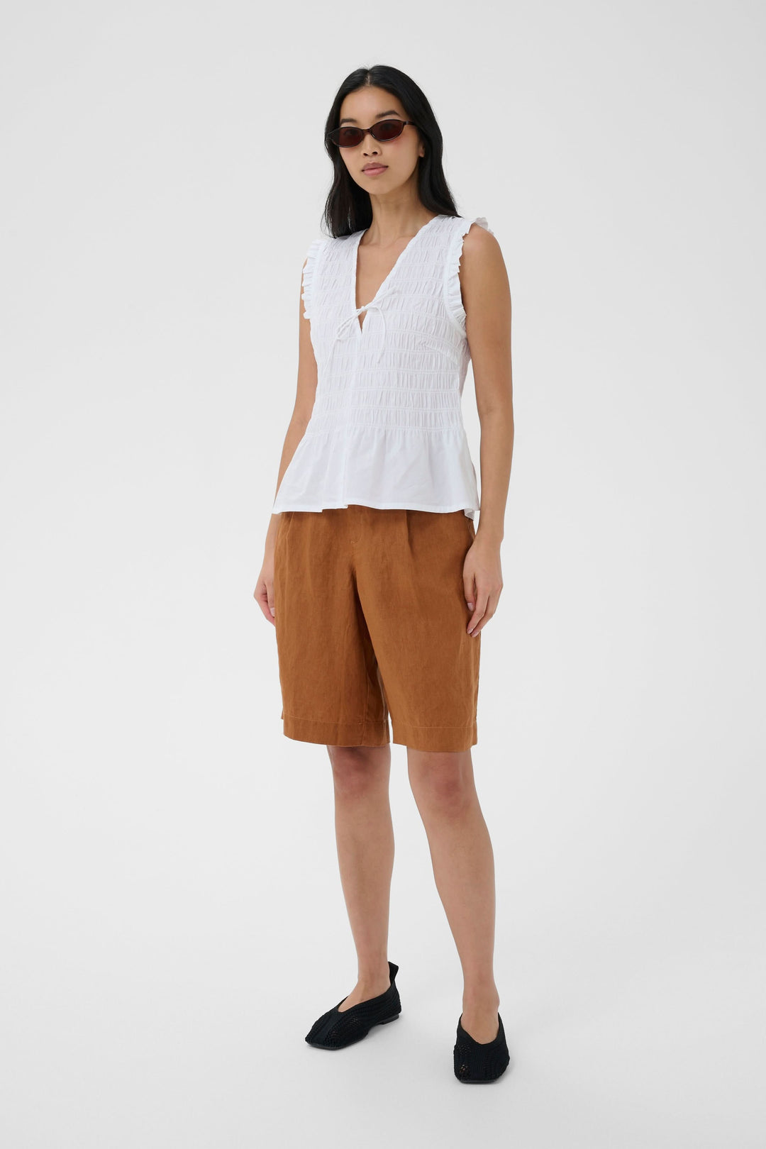 Blouse Borgny smockée sans manches à encolure nouée portée par un mannequin, style estival et féminin, effet smocké, encolure en V.