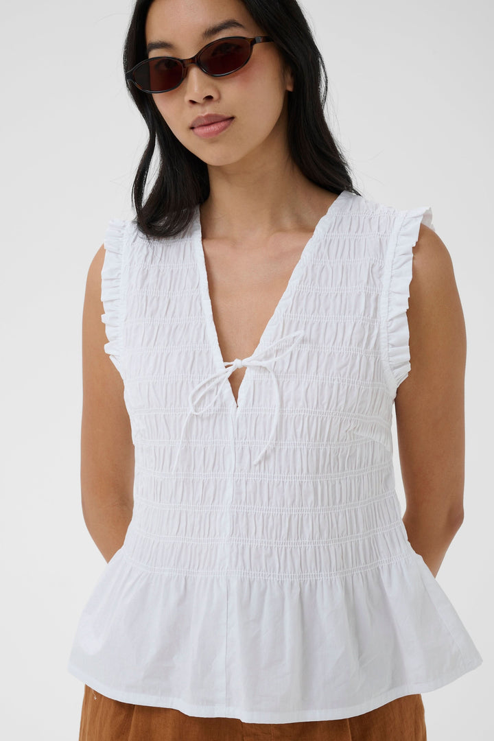 Femme portant une Blouse Borgny smockée sans manches à encolure nouée, idéale pour un style estival délicat et féminin.