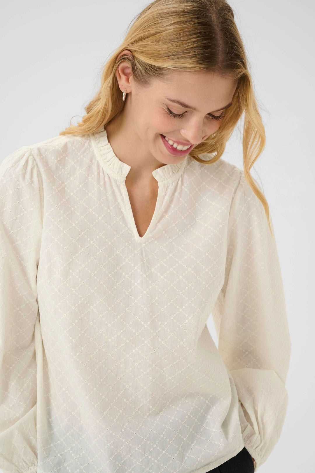 Blouse Eimy chic avec motif discret, encolure fendue et manches bouffantes, portée par un modèle souriant.