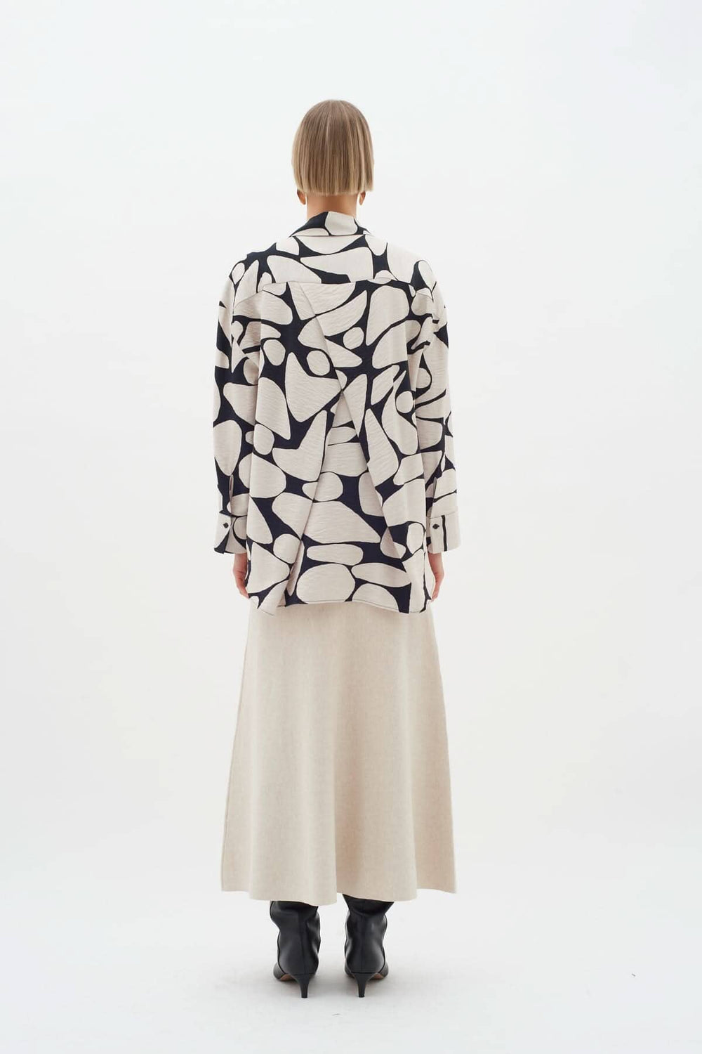Blouse Metta à motifs abstraits vue de dos, portée avec une jupe longue beige et des bottines noires.