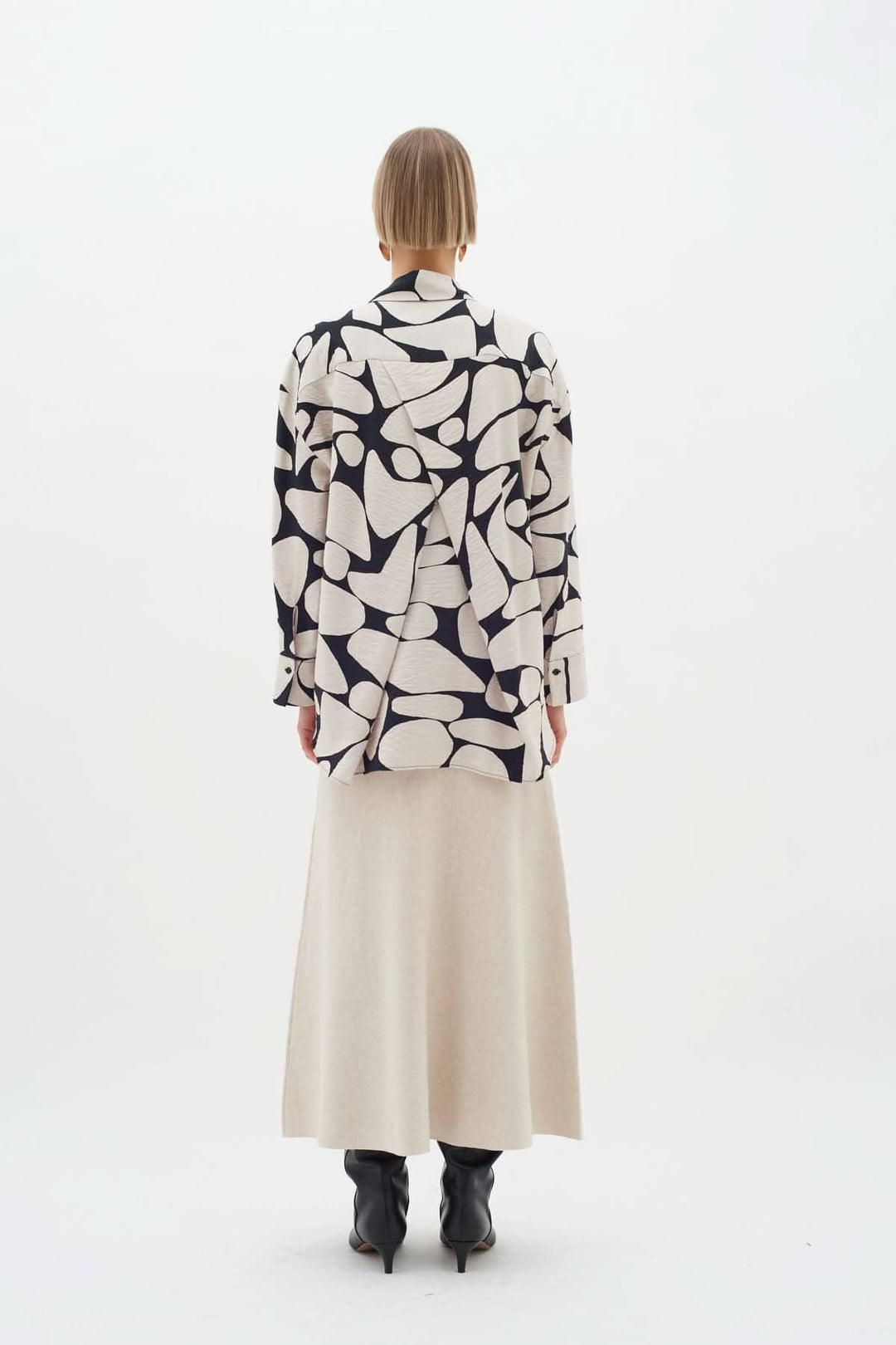 Blouse Metta à motifs abstraits vue de dos, portée avec une jupe longue beige et des bottines noires.