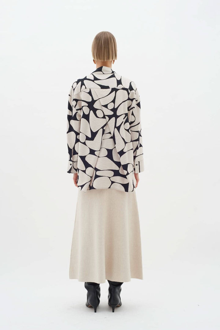 Blouse Metta à motifs abstraits vue de dos, portée avec une jupe longue beige et des bottines noires.