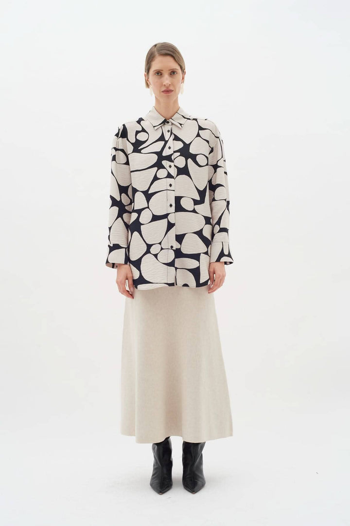 Blouse Metta avec imprimé abstrait, col classique et manches longues, portée par un mannequin avec jupe beige.