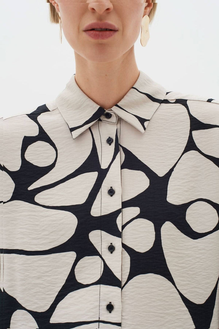 Blouse Metta avec col classique, fermeture boutonnée et imprimé abstrait en noir et blanc.