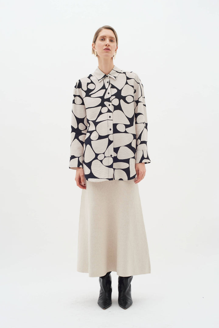 Blouse Metta à col classique, manches longues, imprimé abstrait, portée avec une jupe et des bottes.