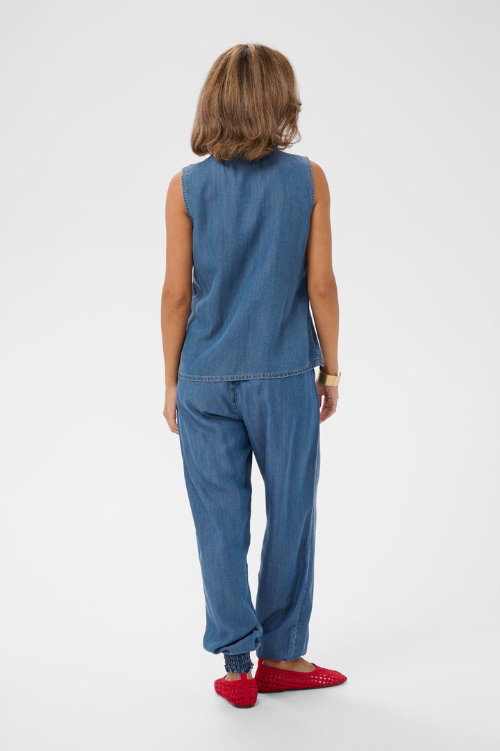Femme portant la Blouse Molly sans manches en denim léger avec un pantalon assorti, vue arrière.