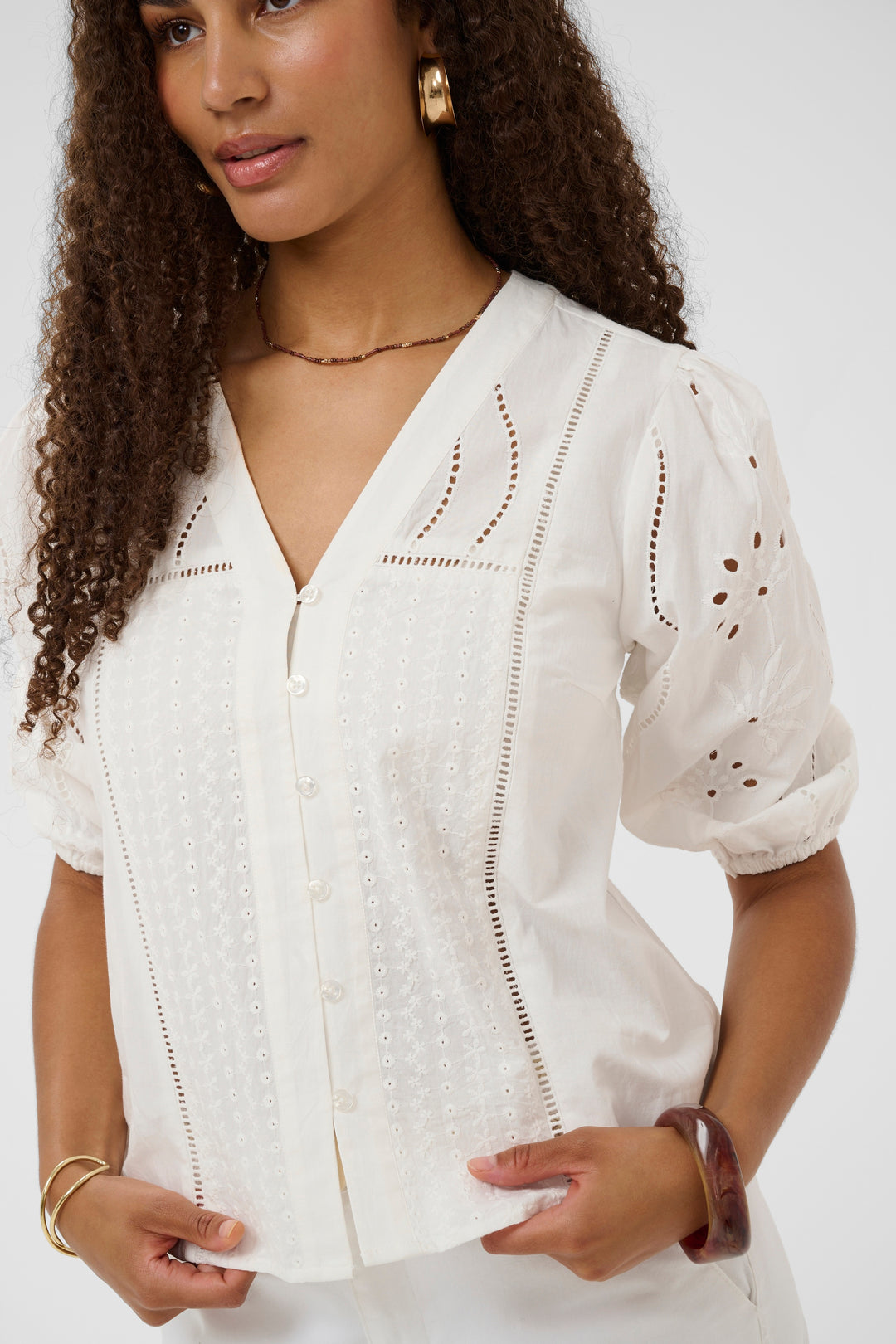 Blouse Signe en blanc avec détails ajourés et broderies délicates, encolure en V, et coupe légèrement fluide pour une élégance raffinée.