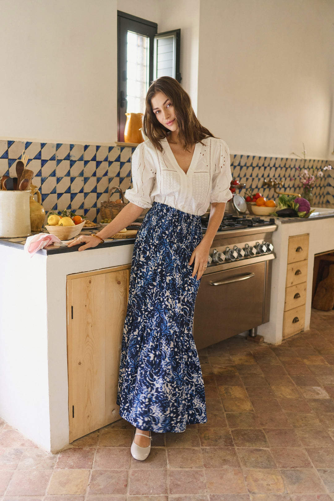 Femme portant Blouse Signe délicate avec détails ajourés et broderies raffinées, encolure en V et coupe fluide, dans une cuisine rustique.