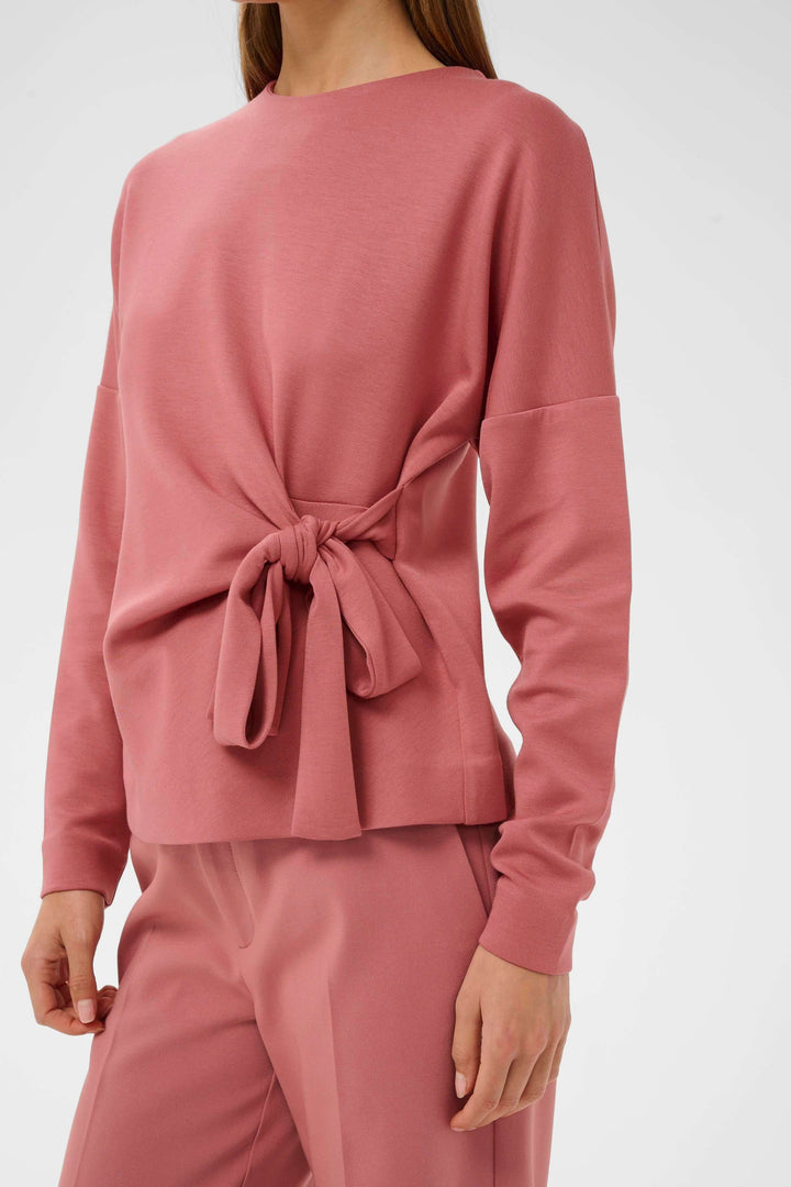Blouse Tricent rose avec détail noué sur le côté, manches longues et coupe flatteuse pour un look contemporain. Mode féminine et structurée.