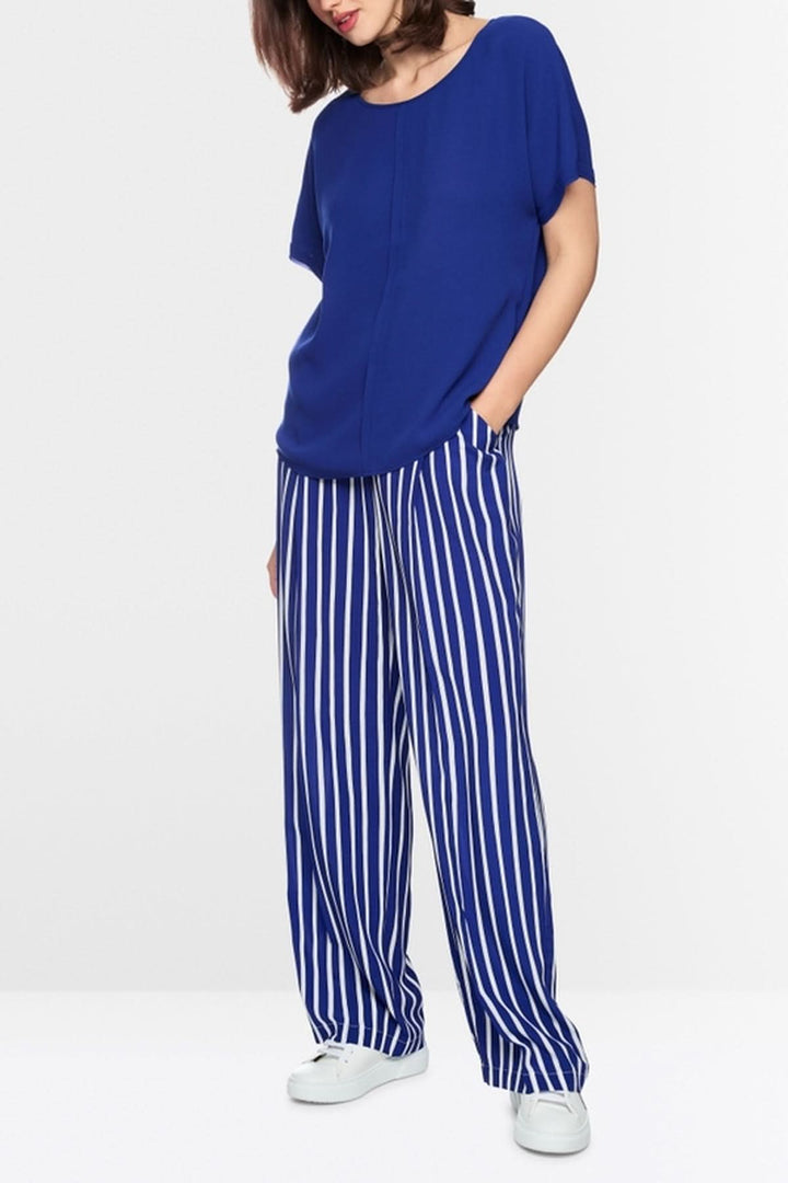 Blouse ample en tissu fluide bleue avec manches courtes, associée à un pantalon rayé, idéale pour une silhouette aérienne et confortable.