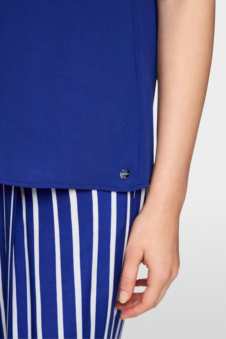Détail de la blouse ample en tissu fluide bleue portée avec pantalon à rayures.