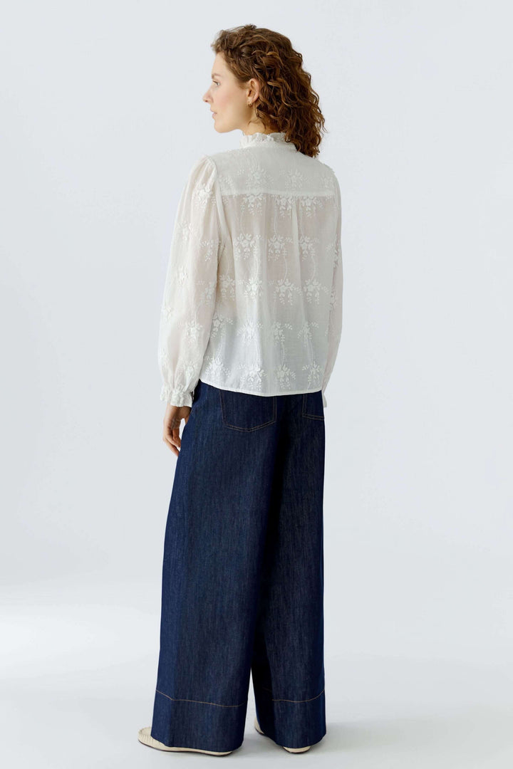 Femme portant une blouse à broderies florales blanche vue de dos, associée à un pantalon large en jean.