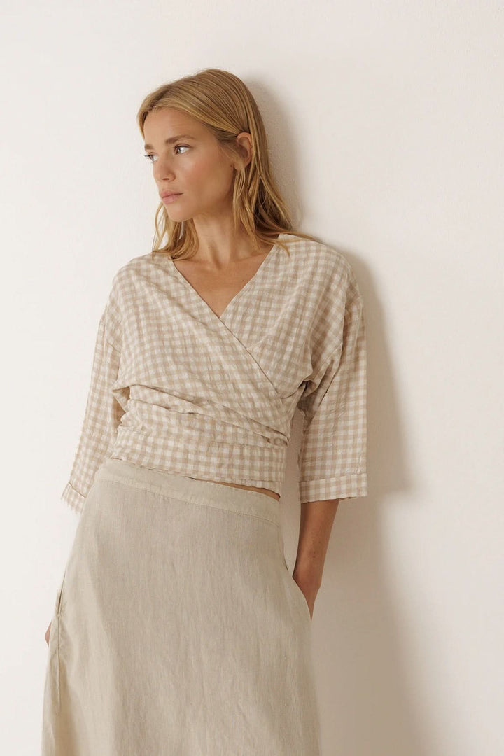 Femme portant une blouse cache-cœur à motif vichy avec manches 3/4, encolure en V croisée et taille ajustée, style élégant et féminin.