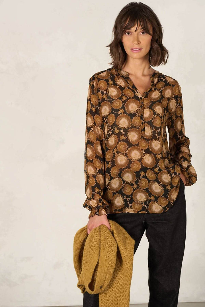 Blouse coupe droite à manches longues avec motif coloré, décolleté en V, portée avec un pull jaune et un pantalon noir.