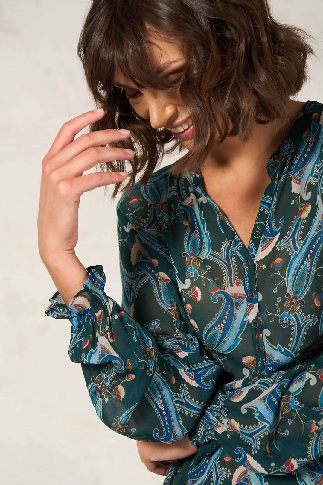 Femme souriante portant une blouse à motifs, avec manches longues et détails élastiques.