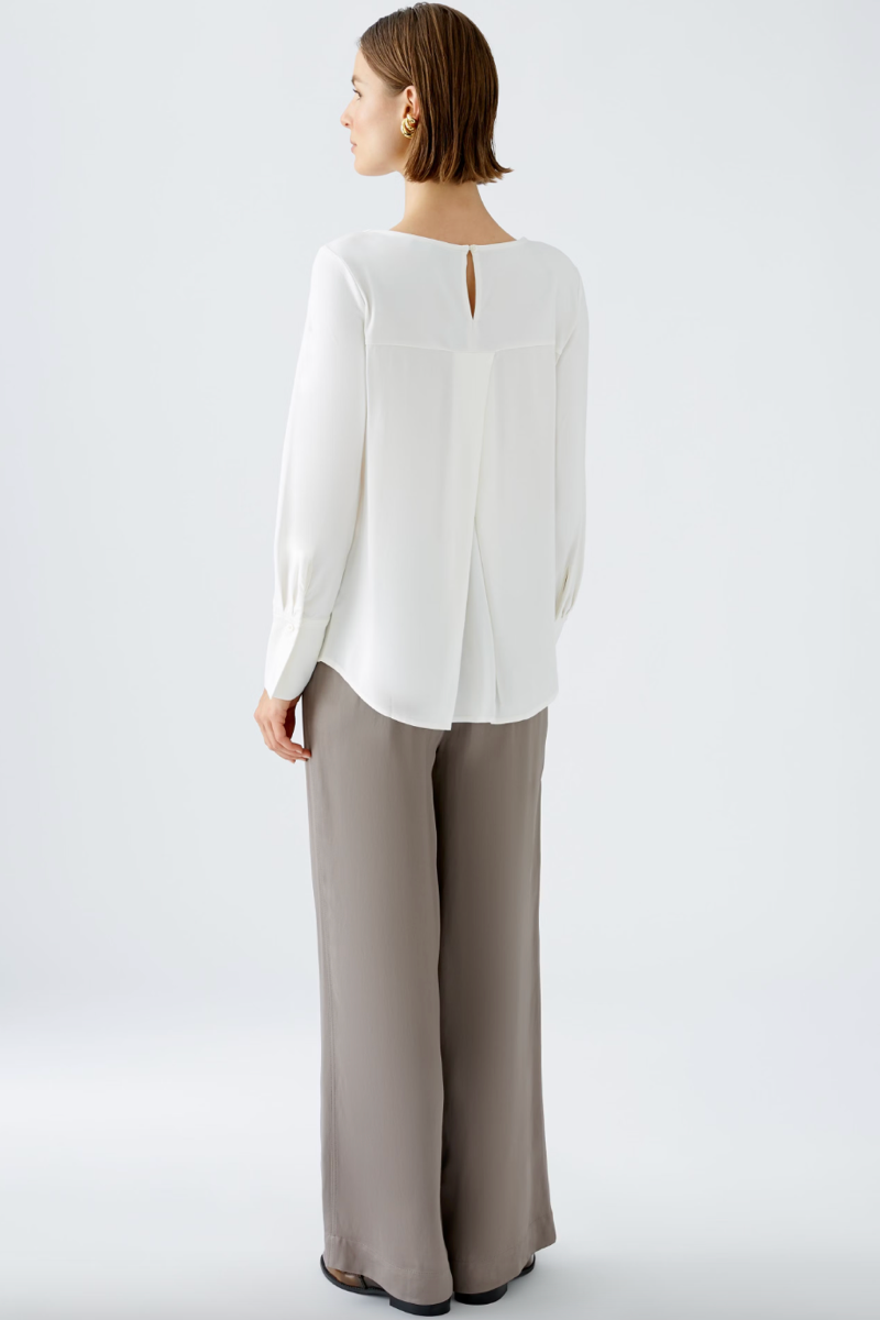 Chemise décontractée blanche avec un col rond et une fente au dos, portée avec un pantalon ample.