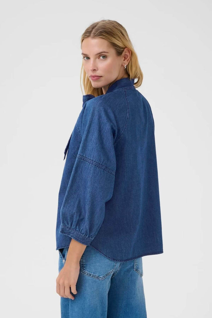 Vue arrière de la blouse en denim avec manches bouffantes et col lavallière, idéale pour un look décontracté et élégant.