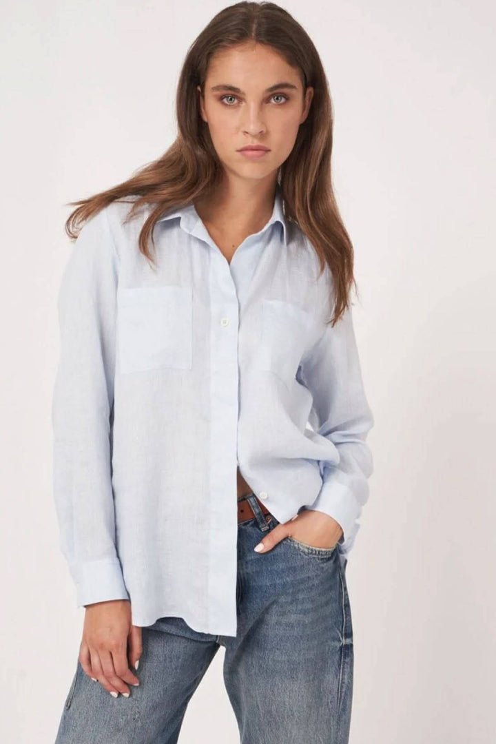 Femme portant une blouse en lin bleu clair avec une coupe droite, manches longues et col classique, style décontracté.