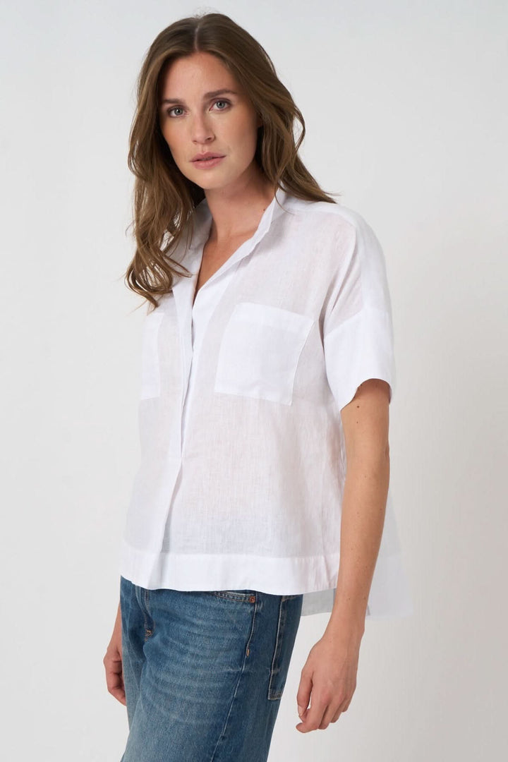 Femme portant une blouse en lin à manches chauve-souris, coupe ample et fluide, avec col chemise ouvert et poche plaquée.