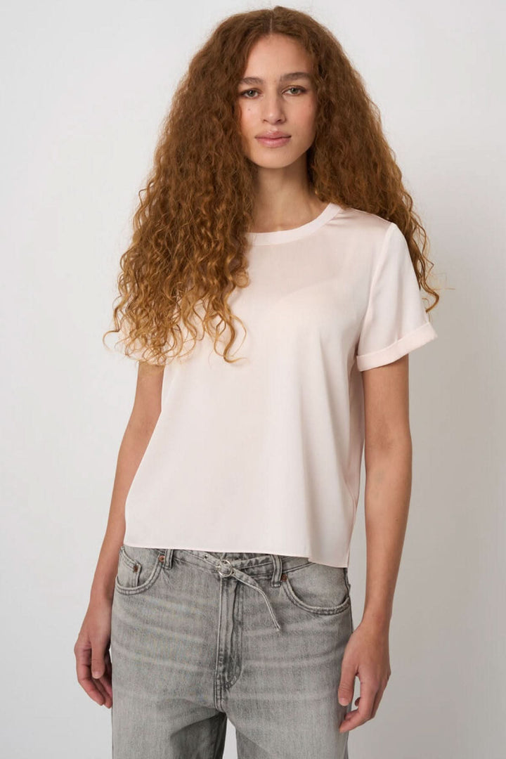 Femme portant une blouse en soie extensible, coupe droite et fluide, manches courtes à revers, look chic et décontracté.