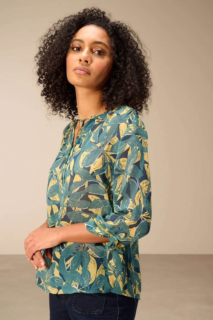 Femme portant une blouse fluide imprimé avec motif végétal et manches 3/4, encolure fendue.
