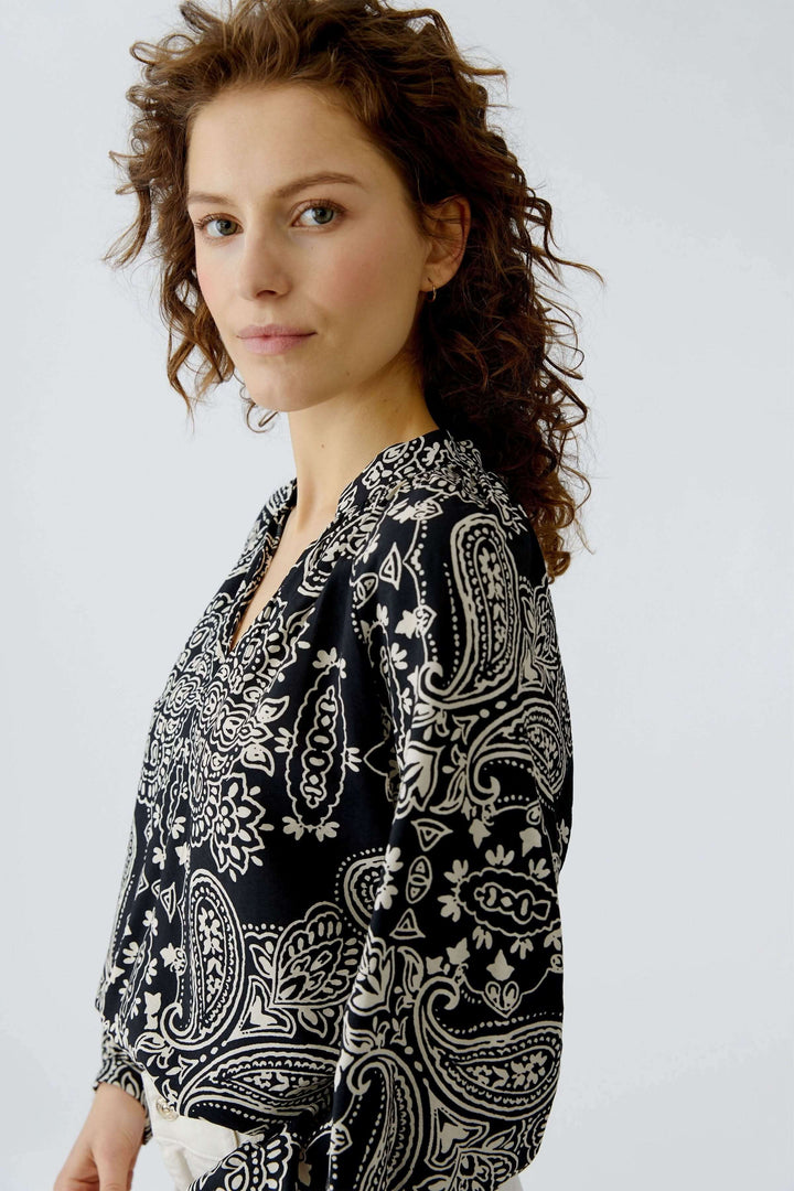 Femme portant une blouse fluide imprimé graphique, coupe droite et encolure ouverte, style bohème chic.