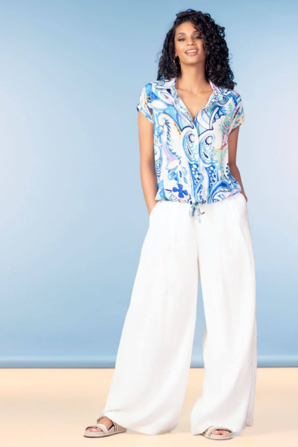 Femme portant une blouse fluide imprimée d’inspiration artistique avec un pantalon blanc ample.