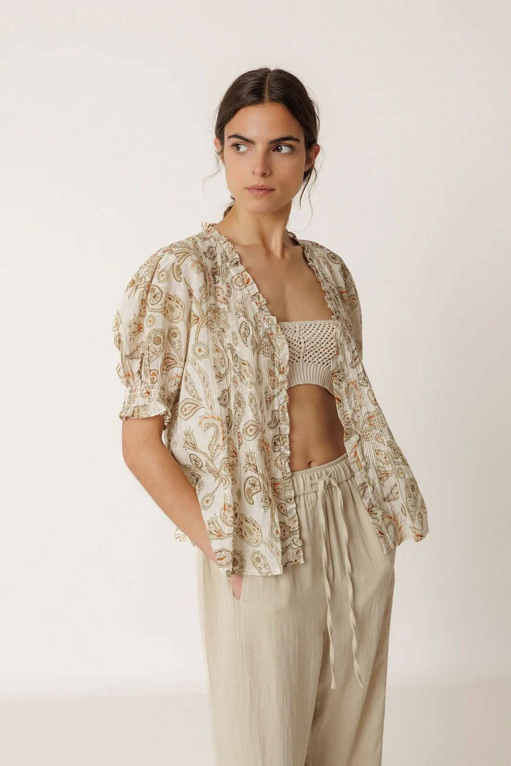 Blouse fluide imprimée à manches courtes avec motifs délicats, portée par un mannequin, mettant en valeur les manches courtes et encolure travaillée.