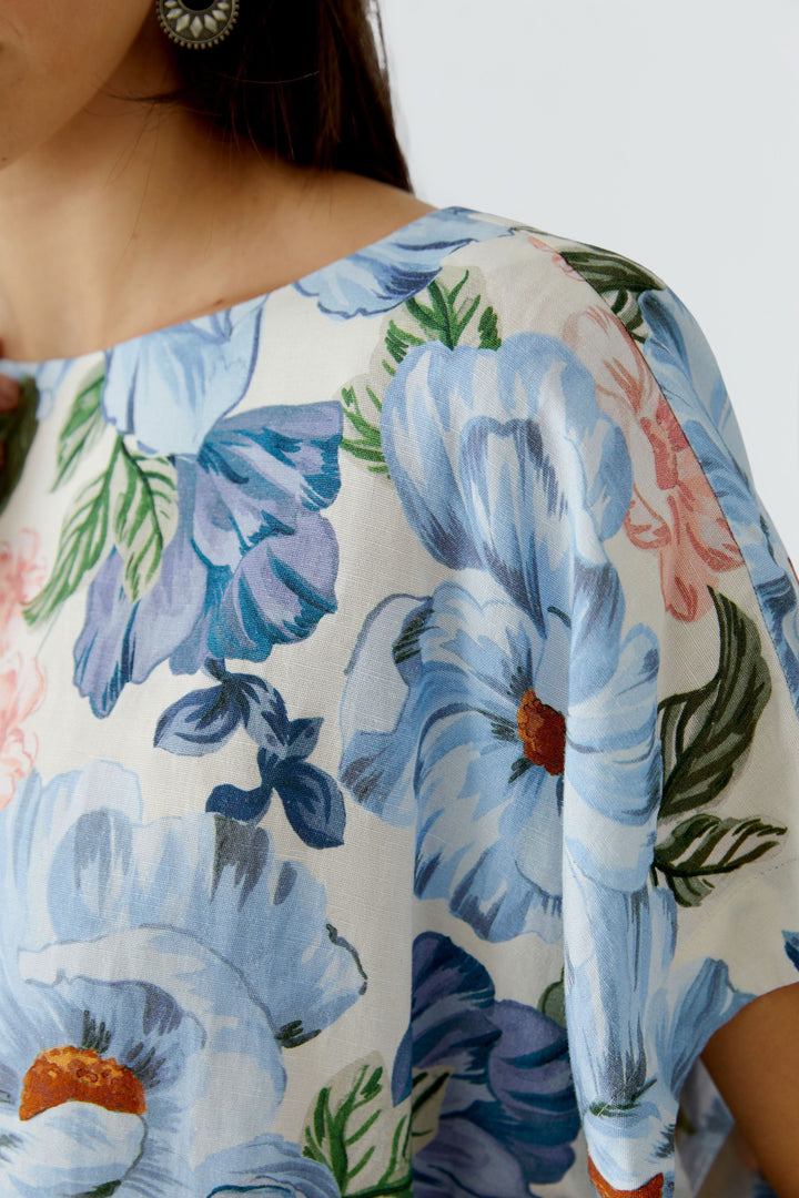 Blouse fluide à manches courtes avec motif floral bleu et rose, encolure arrondie, tissu léger reflétant élégance et confort.