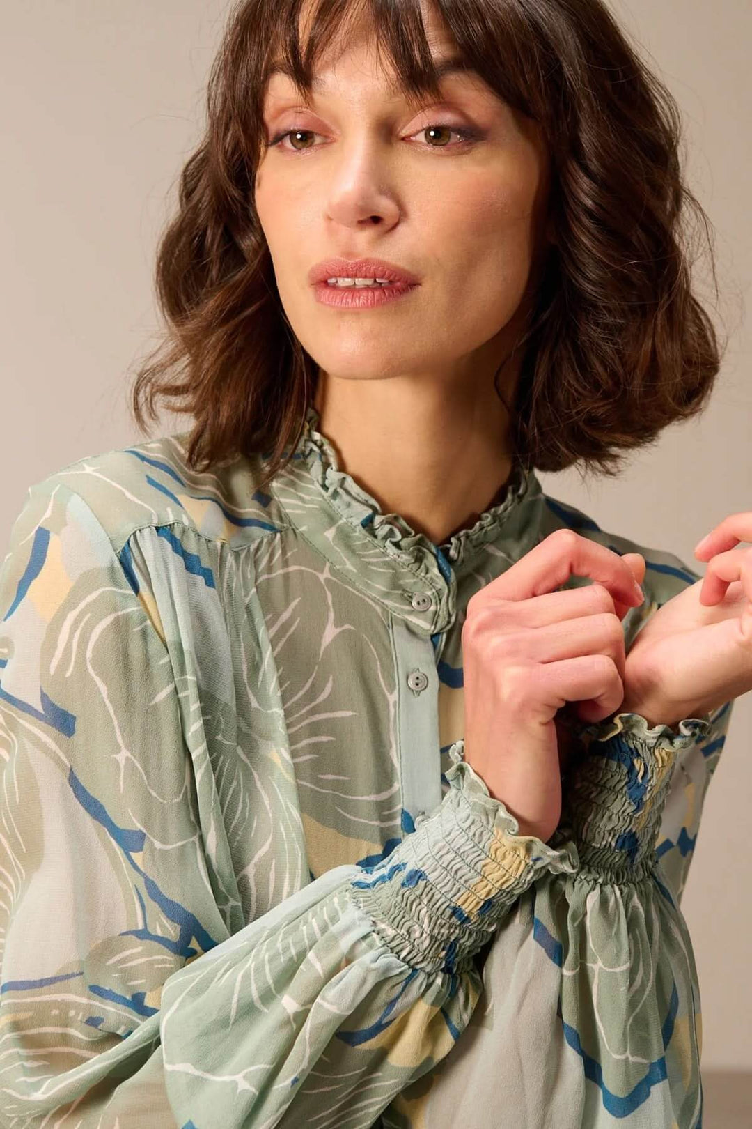 Femme portant une blouse fluide à manches longues avec col montant et tissu imprimé léger.