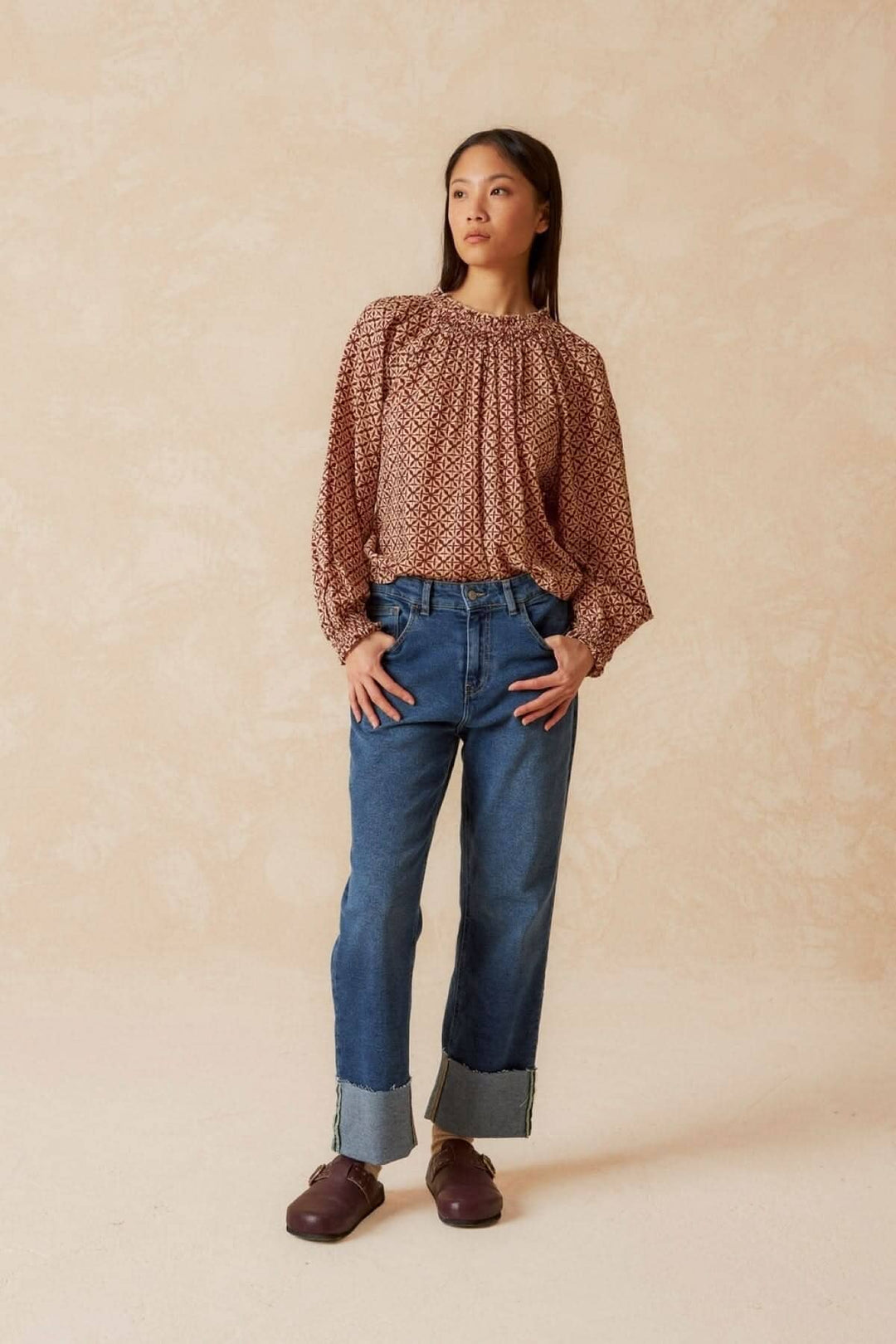 Femme portant une blouse imprimée mosaïque, manches longues, associée à un jean bleu, look moderne et chic.