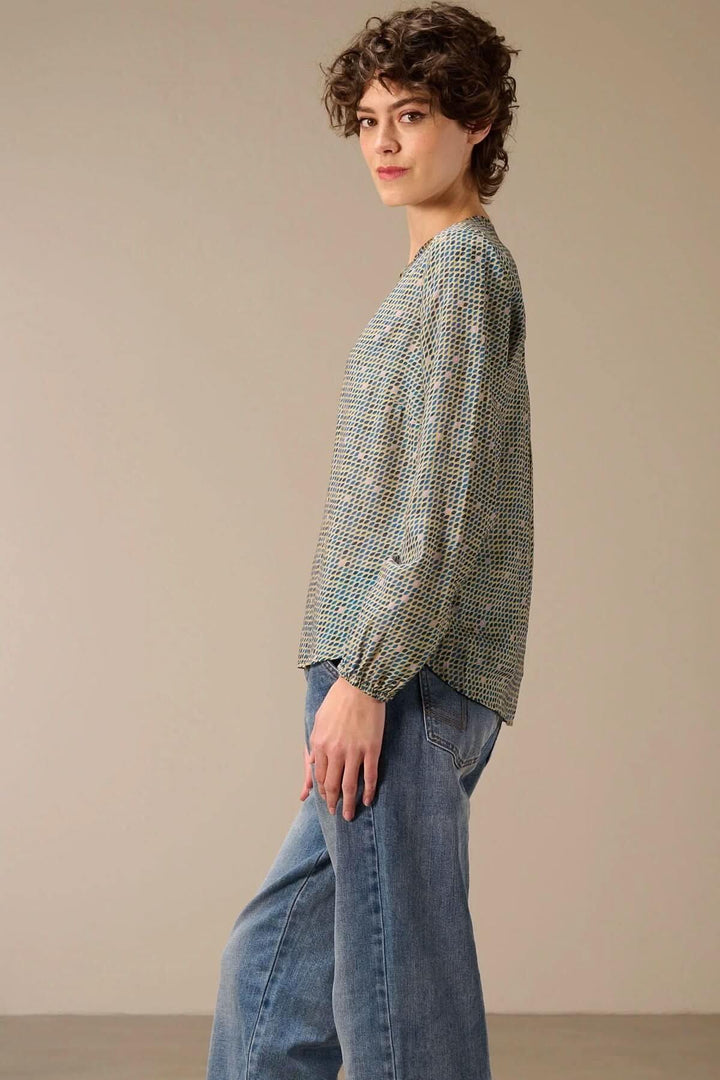 Femme portant une blouse imprimée à manches longues avec un look décontracté et moderne, associée à un jean bleu.