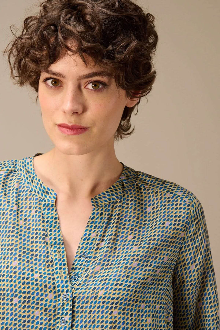 Femme portant une blouse imprimée à manches longues avec encolure fendue, aspect graphique subtil et coupe décontractée.