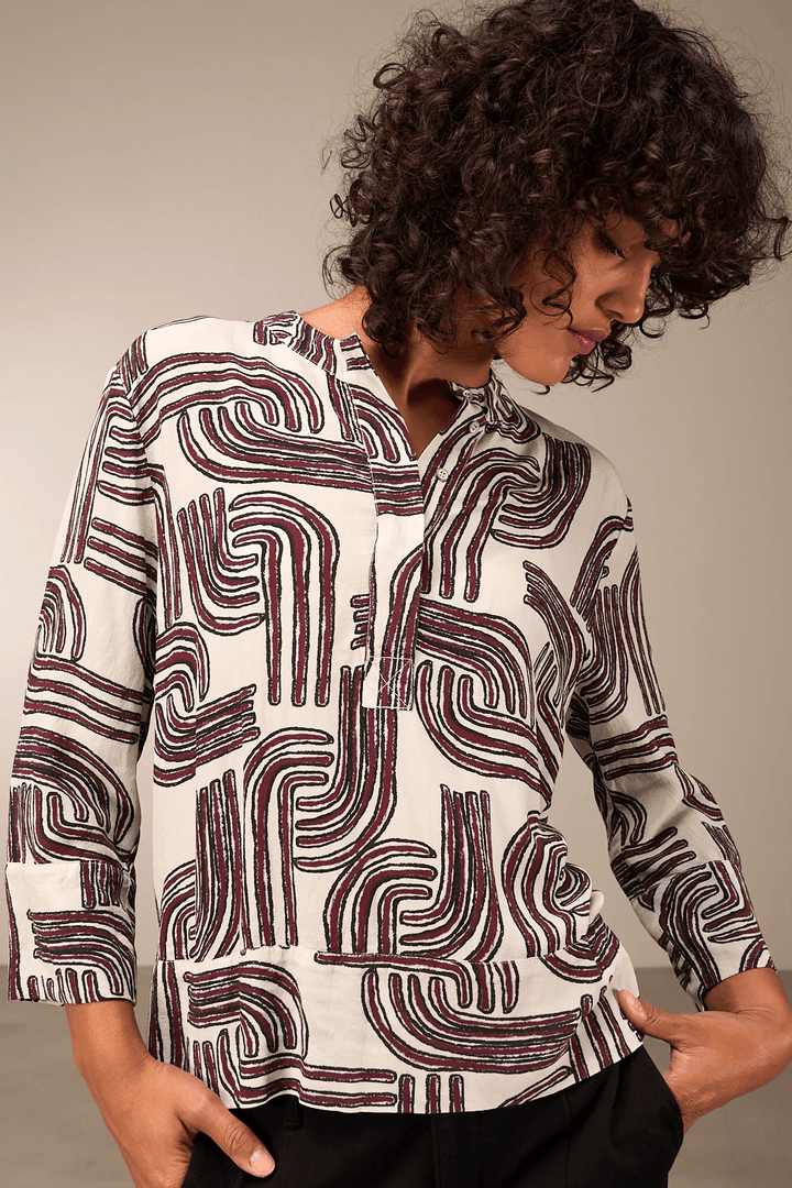 Femme portant une blouse à manches 3/4 avec motif graphique, encolure ronde et coupe décontractée pour un look moderne et élégant.