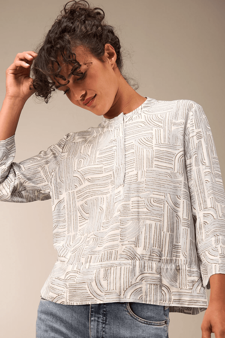 Femme portant une blouse à manches 3/4 avec motif, encolure ronde et patte boutonnée, idéale pour un style moderne décontracté.