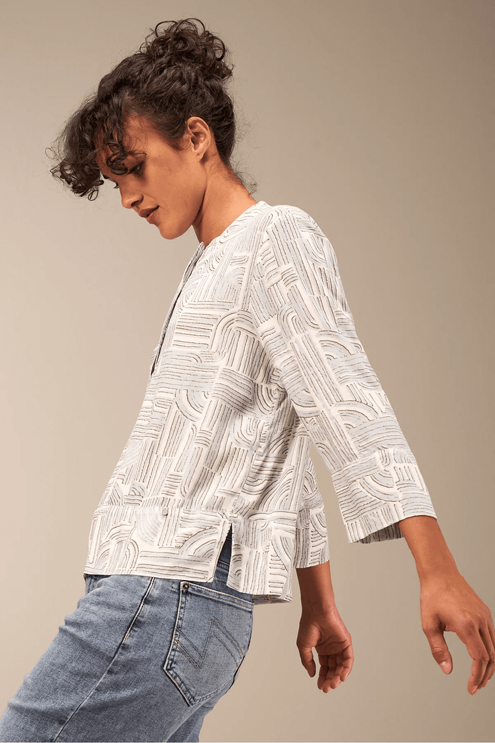 Femme portant une blouse à manches 3/4 avec motif fluide, encolure ronde et coupe décontractée, assortie d'un jean pour un style moderne.