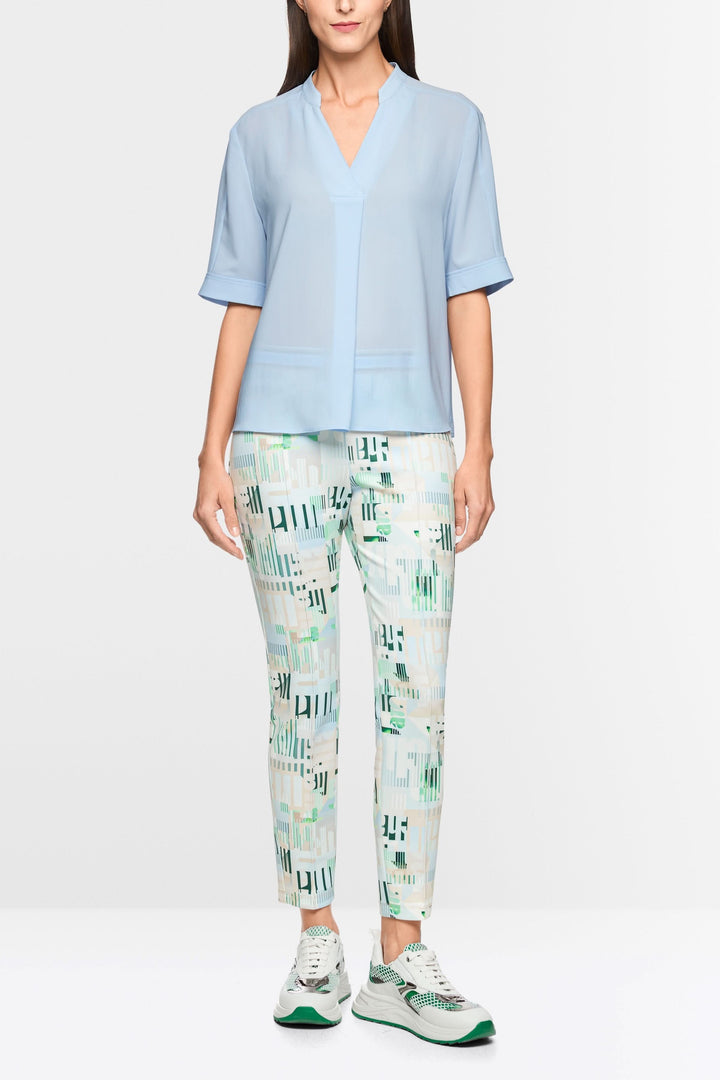 Modèle portant une blouse à manches courtes bleue avec un col V élégant et des manches à revers, associée à un pantalon imprimé.