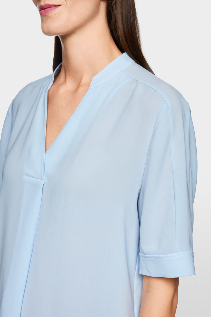 Blouse à manches courtes avec encolure en V et tissu fluide bleu clair, mise en valeur pour son style moderne et épuré.