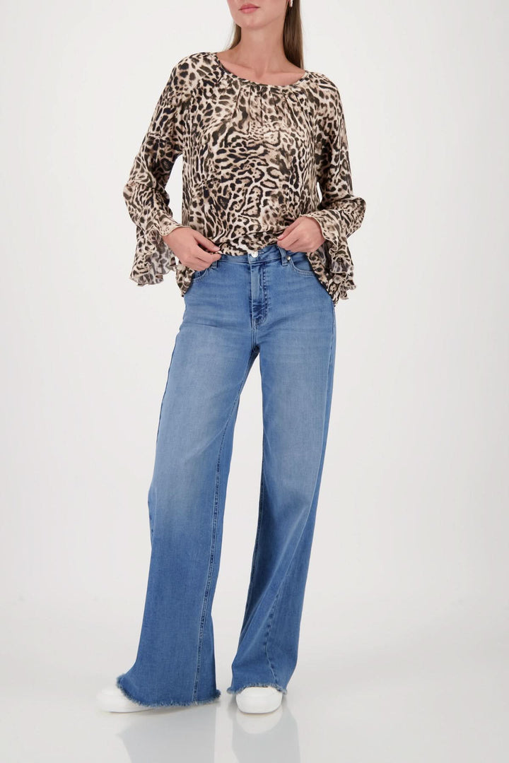 Blouse à motif léopard avec encolure ronde et manches évasées, portée avec un jean large pour un look décontracté et élégant.