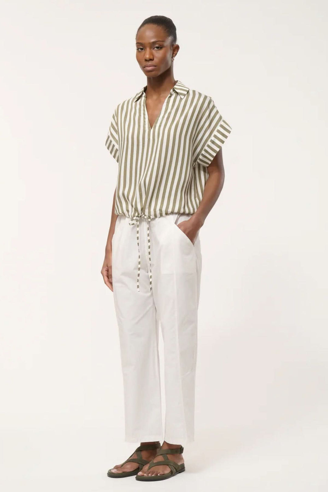 Femme portant une blouse rayée à col avec pantalon blanc ample et sandales, silhouette fluide et contemporaine.