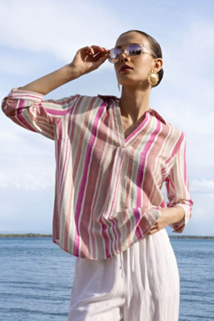 Blouse rayée à encolure V pour femme, fluide et élégante, avec manches trois-quarts et rayures verticales, portée en bord de mer.