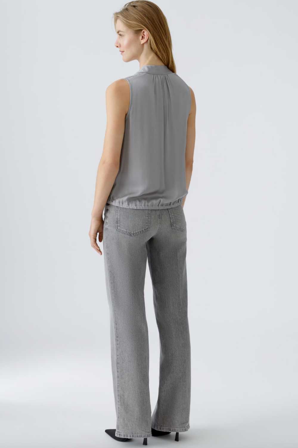 Femme de dos portant une blouse satinée grise et un pantalon gris, style décontracté et élégant.