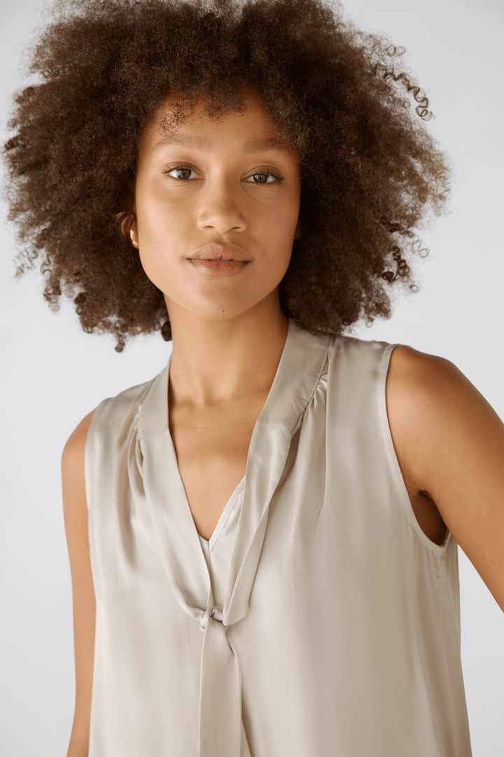 Détail blouse évasée avec texture satinée et volants pour volume et allure féminine raffinée, encolure en V fermée par rabat.